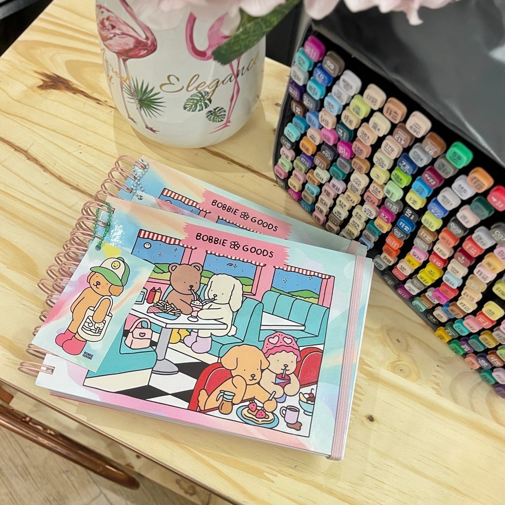 Livros de colorir Bobbie Goods ao lado de um estojo com canetinhas coloridas organizadas, prontos para pintar.