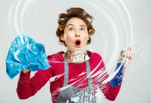 Mulher surpresa limpando vidro com pano azul e spray de limpeza.