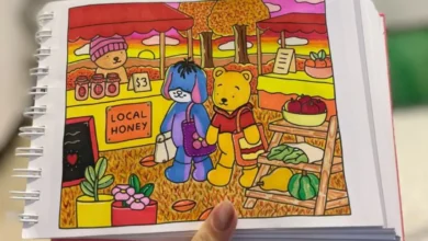 Ilustração colorida de dois personagens de pelúcia, um urso e um cachorro, em um mercado ao ar livre com barracas de mel e frutas. Eles estão caminhando por entre flores e vegetação no outono.