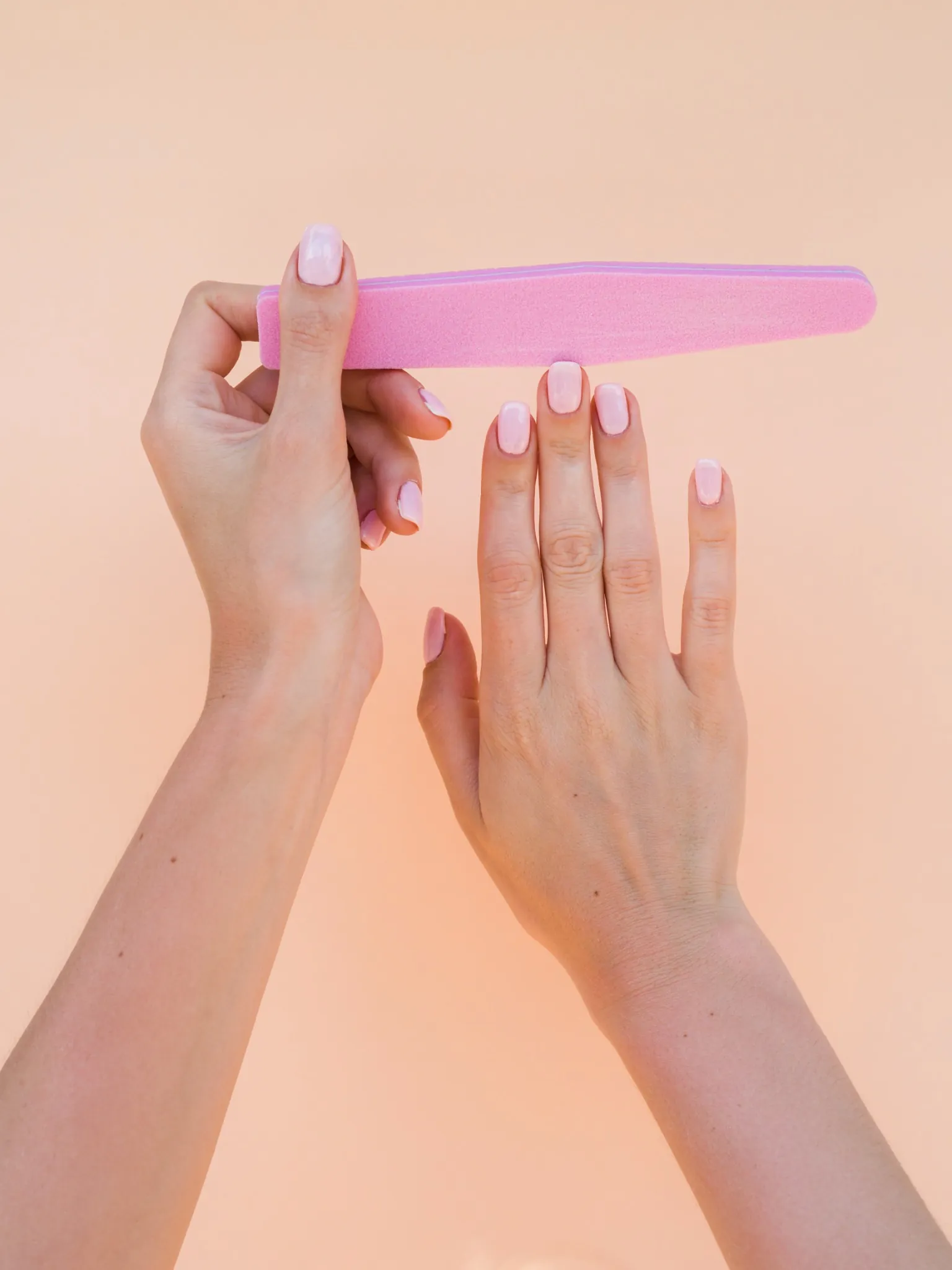 Mãos femininas lixando unhas com lixa rosa