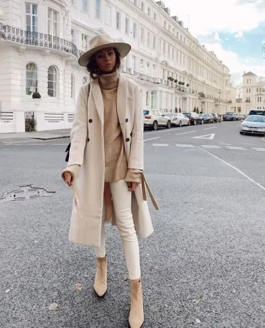 Mulher usando look monocromático de tons neutros com casaco claro, suéter e botas de camurça.
