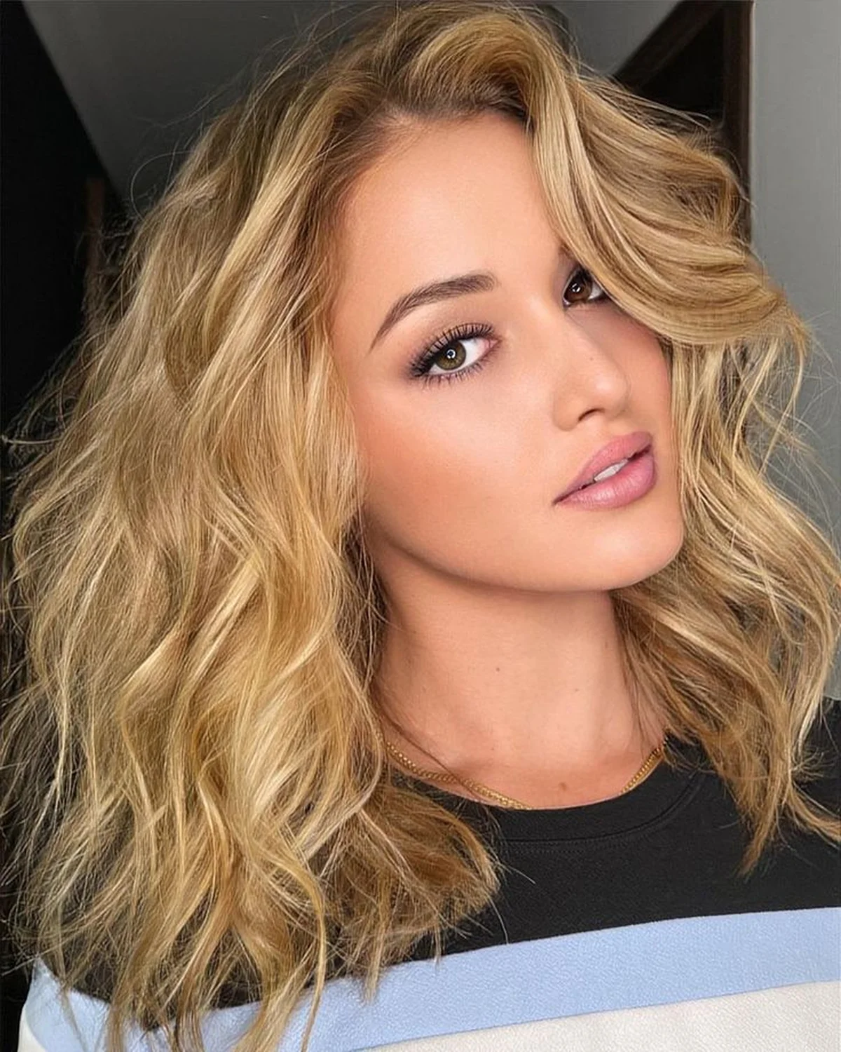 Mulher com cabelo loiro dourado em corte médio, com ondas soltas e acabamento iluminado.