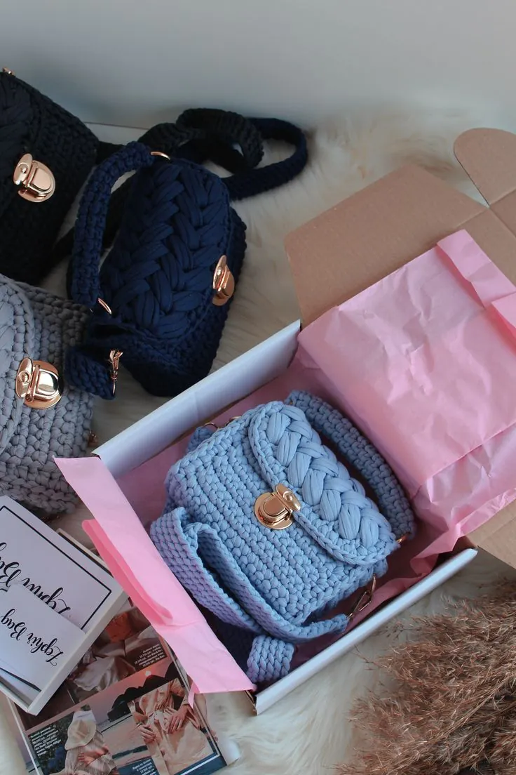 Mini bolsas de crochê coloridas com fecho dourado, uma delas em caixa de presente