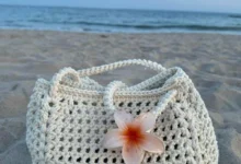 Bolsa de crochê com flor de plumeria em fundo de praia