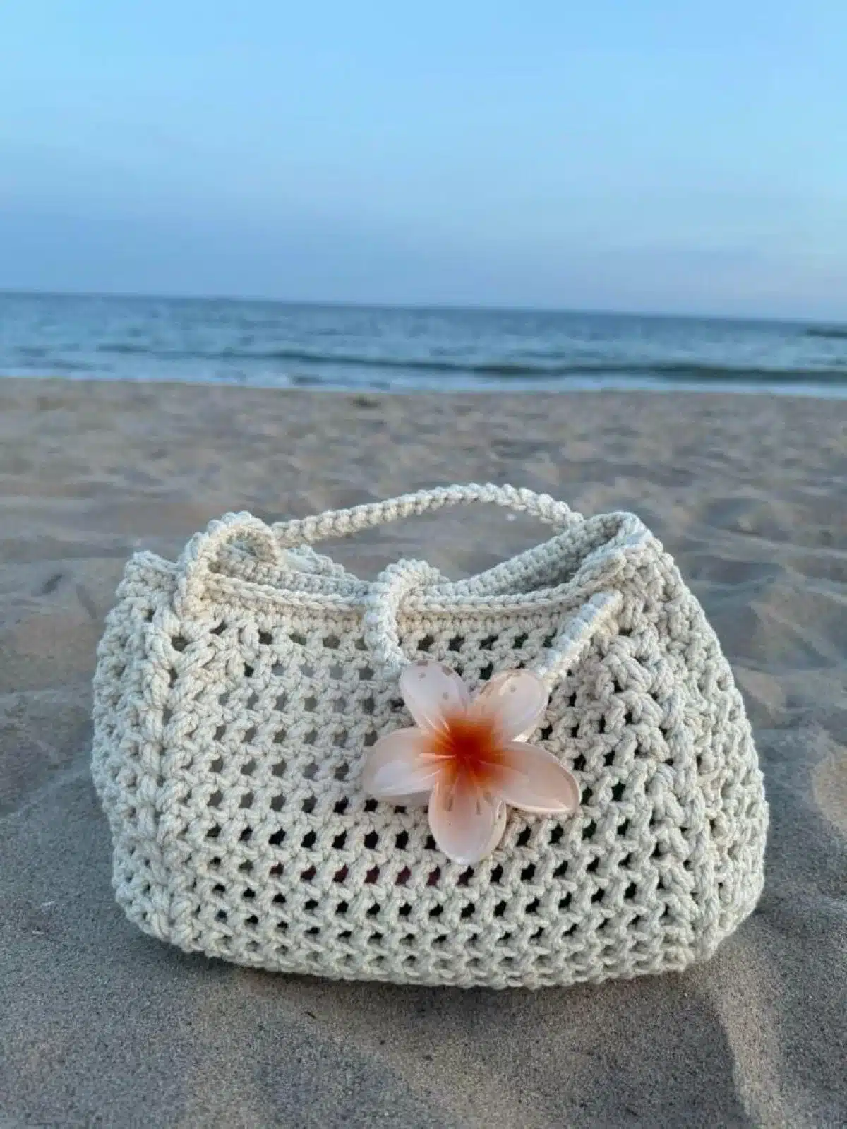 Bolsa de crochê com flor de plumeria em fundo de praia