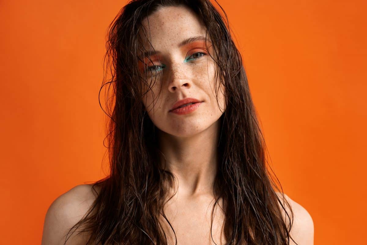 Mulher com cabelo molhado e maquiagem vibrante, com sobrancelhas grossas, destacando a tendência de cabelo molhado para 2025.