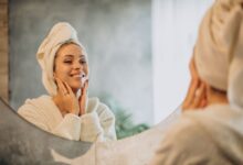 Mulher sorrindo em frente ao espelho enquanto cuida da pele após o banho