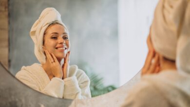 Mulher sorrindo em frente ao espelho enquanto cuida da pele após o banho