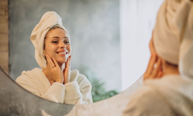 Mulher sorrindo em frente ao espelho enquanto cuida da pele após o banho