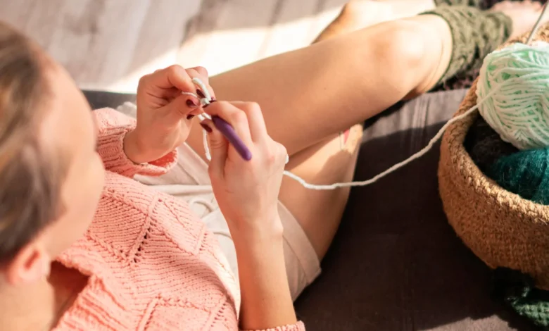 Mulher crochetando com fio branco, criando pontos em um ambiente aconchegante e ensolarado.