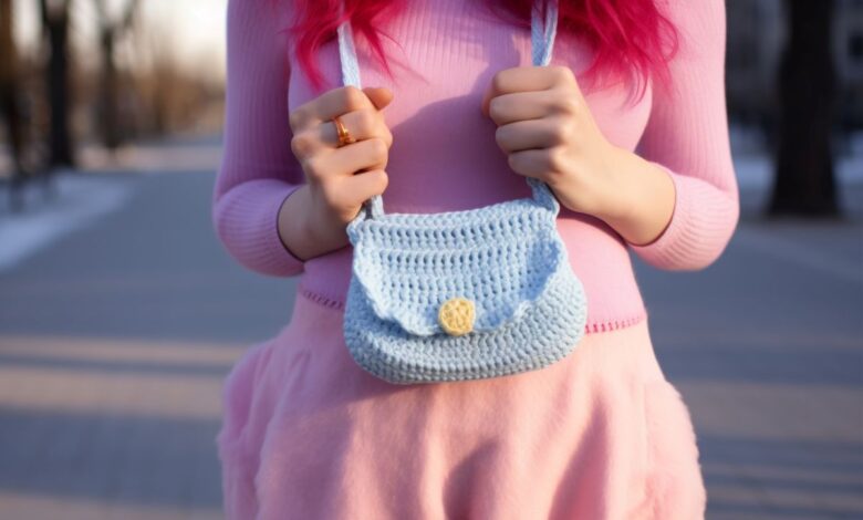 Mulher com cabelo rosa usando uma bolsa de crochĂȘ azul com botĂŁo amarelo, em ambiente externo.