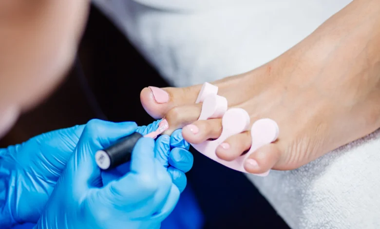 Aplicação de esmalte de gel rosa claro em unhas dos pés, um processo de pedicure profissional.