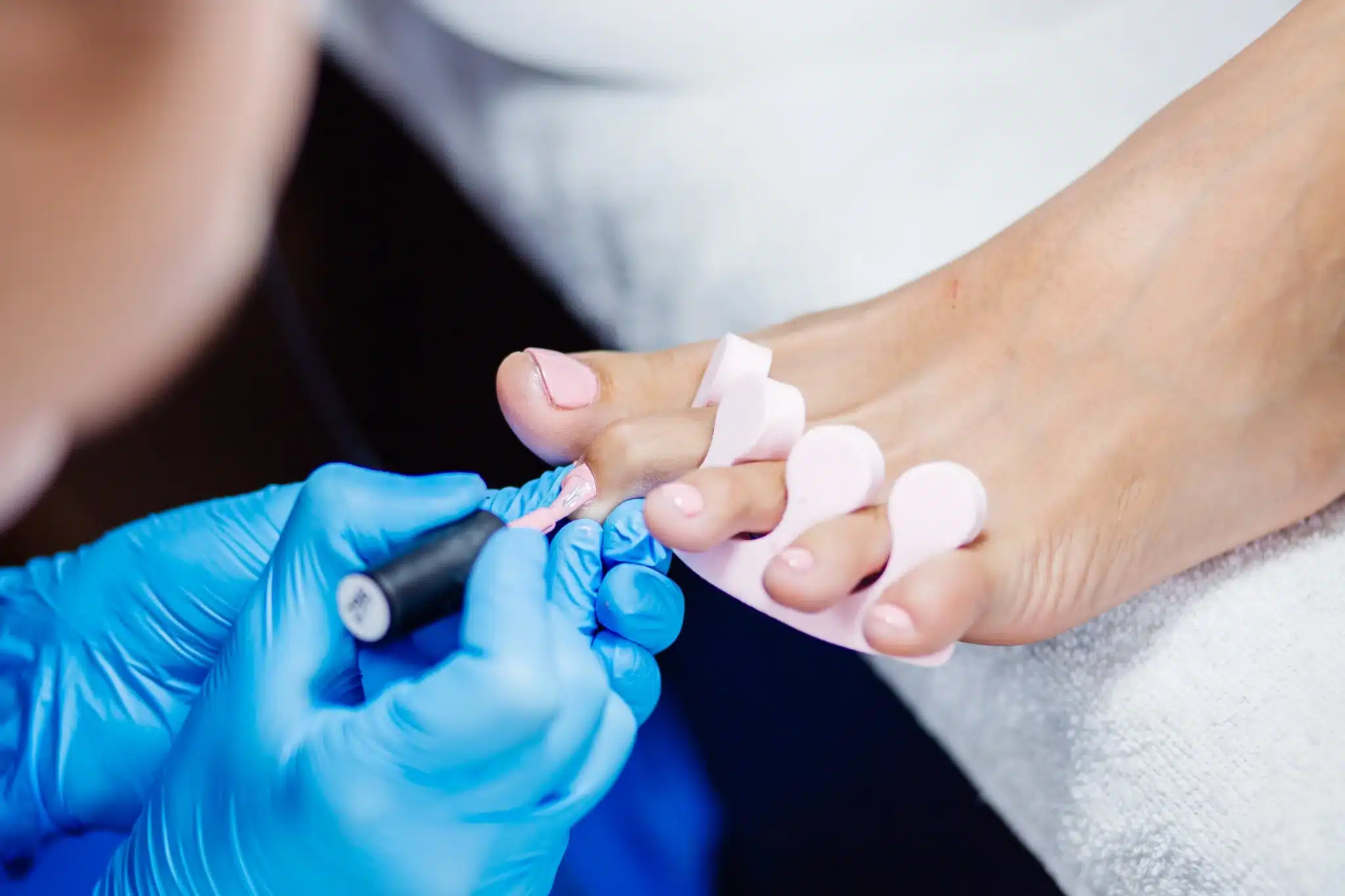 Aplicação de esmalte de gel rosa claro em unhas dos pés, um processo de pedicure profissional.