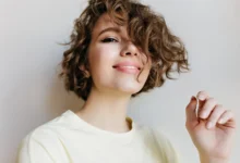 Mulher sorrindo com cabelo cacheado, usando camiseta amarela, destacando penteado moderno para cabelo curto.