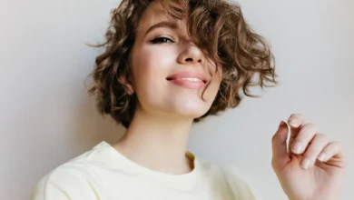 Mulher sorrindo com cabelo cacheado, usando camiseta amarela, destacando penteado moderno para cabelo curto.