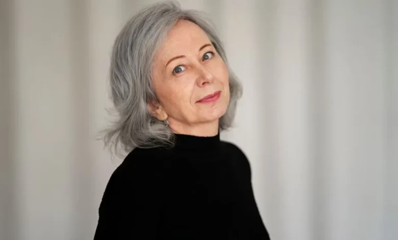 Mulher de cabelo curto grisalho, usando blusa preta, com expressão suave e confiante.