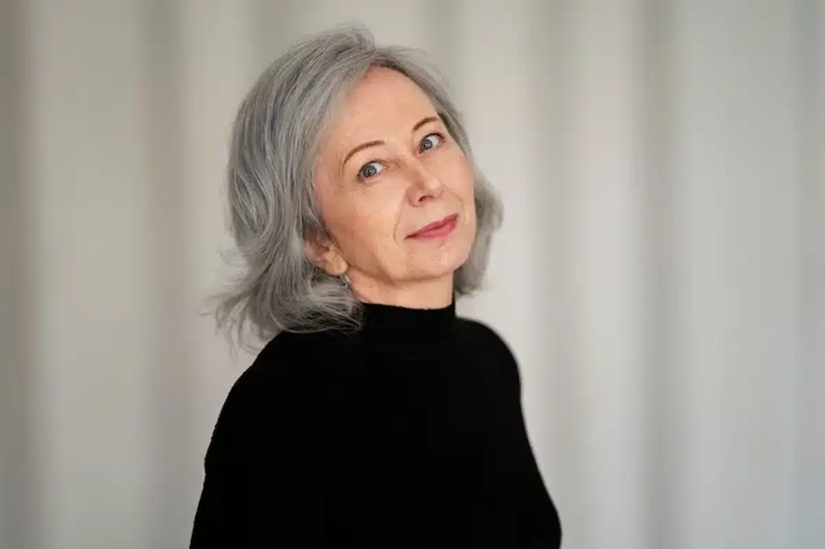 Mulher de cabelo curto grisalho, usando blusa preta, com expressão suave e confiante.