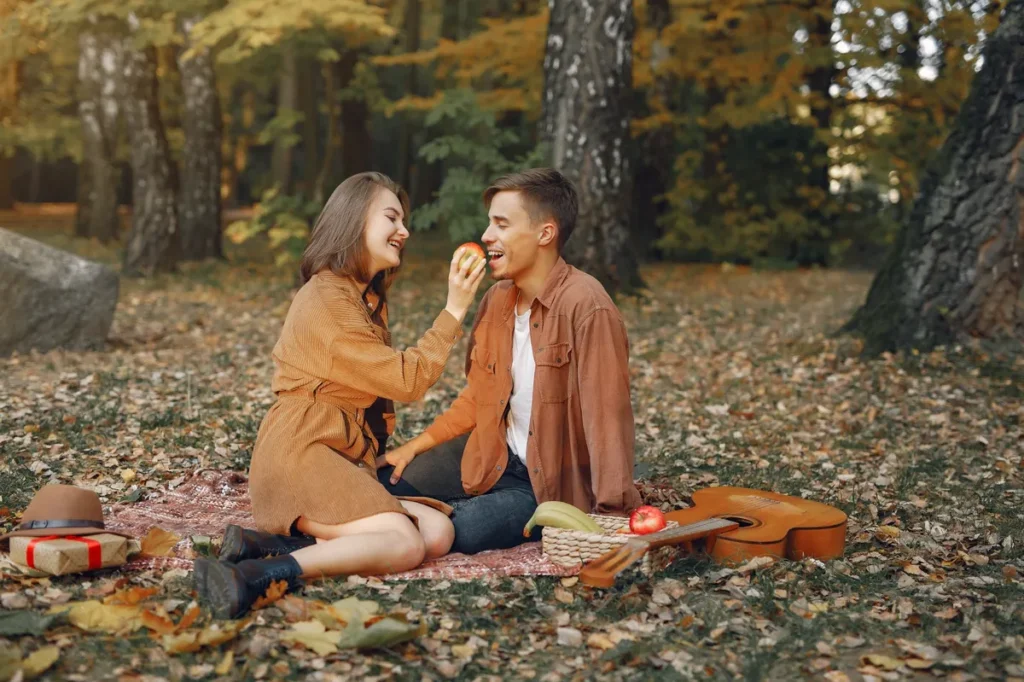 Casal fazendo piquenique ao ar livre em parque de outono, compartilhando maçã e momentos de conexão