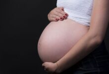 Mulher grávida segurando a barriga com fundo escuro
