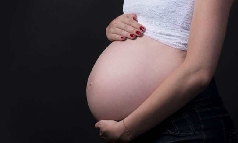 Mulher grávida segurando a barriga com fundo escuro