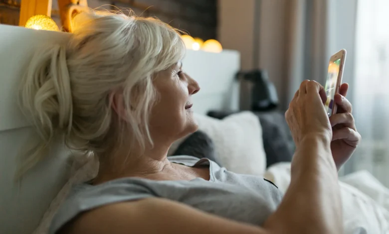 Mulher madura relaxando na cama enquanto usa o celular