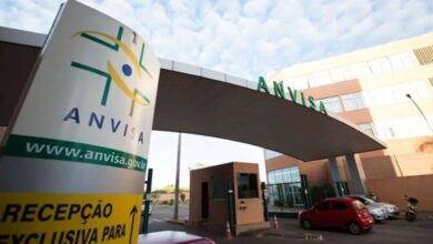Entrada da sede da Anvisa com placa de recepção e carros estacionados.