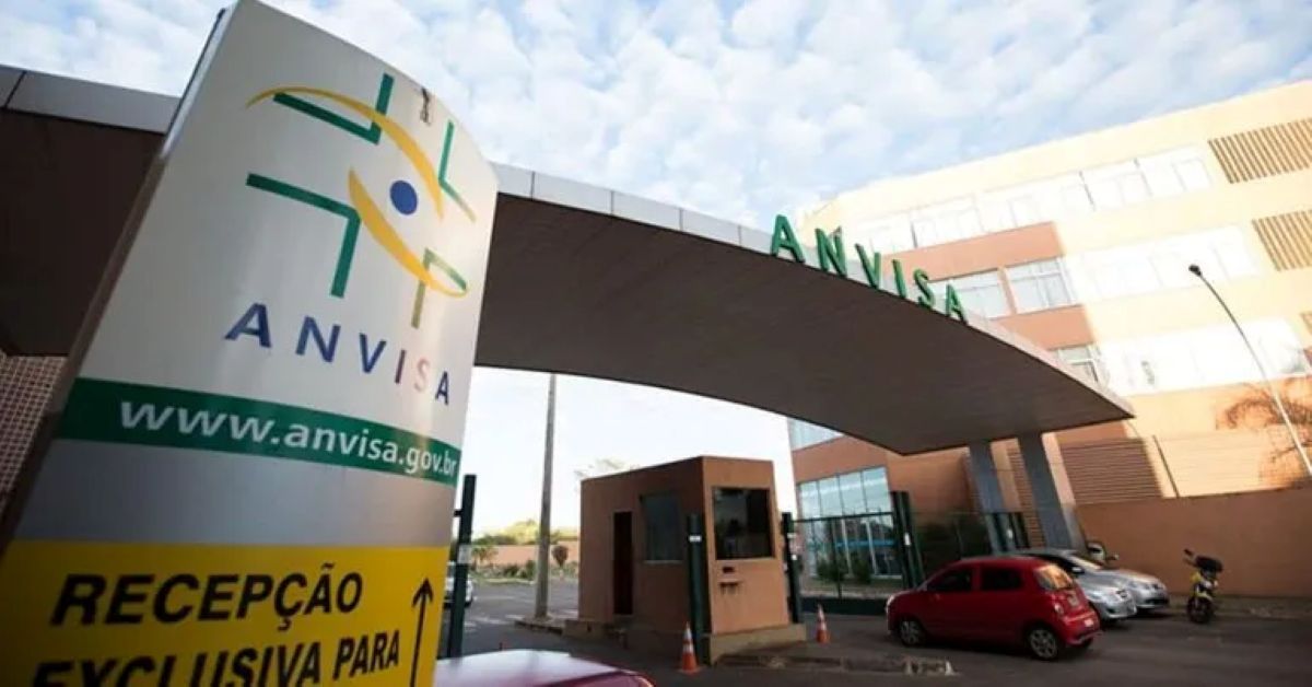 Entrada da sede da Anvisa com placa de recepção e carros estacionados.