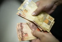 Pessoa segurando cédulas de reais, representando o pagamento da segunda parcela do 13º salário do INSS