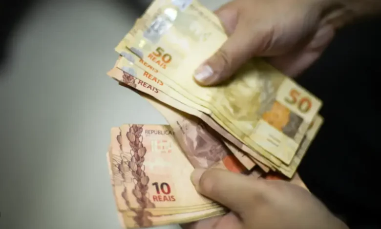 Pessoa segurando cédulas de reais, representando o pagamento da segunda parcela do 13º salário do INSS