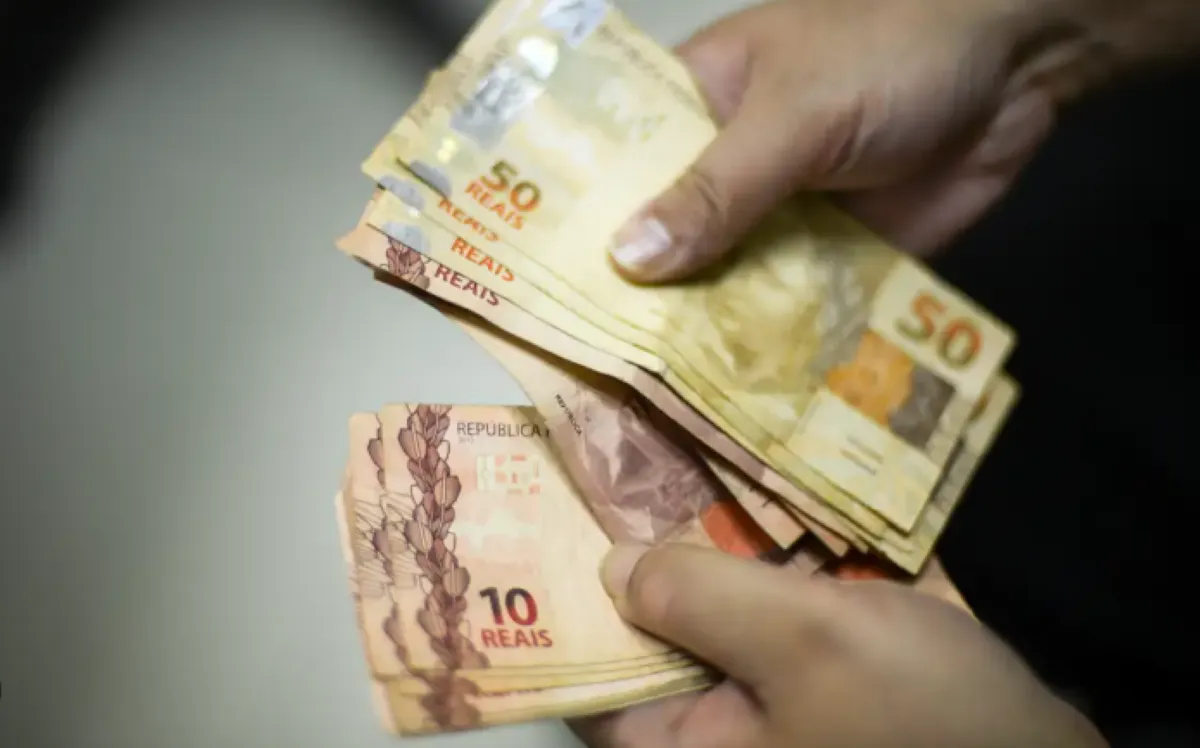 Pessoa segurando cédulas de reais, representando o pagamento da segunda parcela do 13º salário do INSS