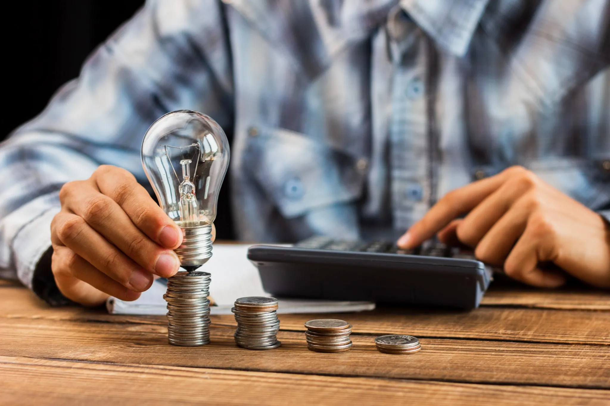 Pessoa segurando uma lâmpada sobre pilhas de moedas, representando economia de energia e finanças pessoais.