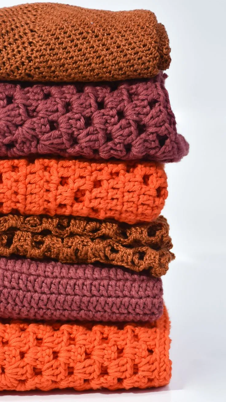 Conjunto de peças de crochê em diferentes texturas, empilhadas em tons de laranja e roxo, mostrando a diversidade de padrões.