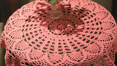 Toalha de crochê rosa sobre mesa redonda com vaso de folhas verdes ao centro
