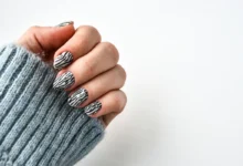 Unhas com esmalte preto e branco em padrão zebra, com suéter cinza de lã.
