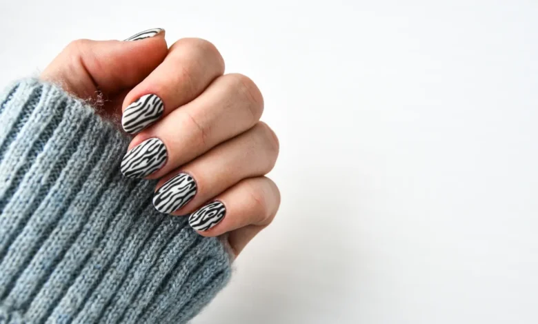 Unhas com esmalte preto e branco em padrão zebra, com suéter cinza de lã.