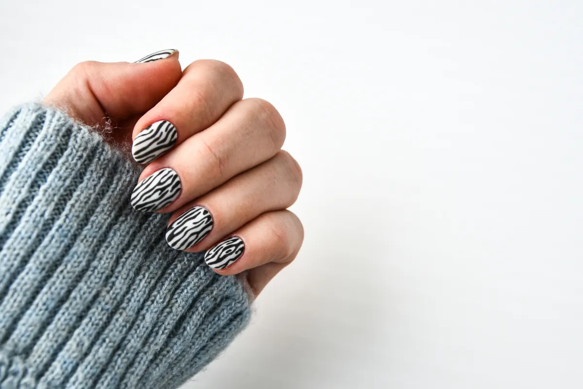Unhas com esmalte preto e branco em padrão zebra, com suéter cinza de lã.