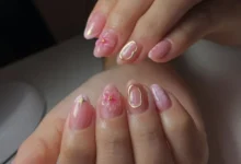 Unhas decoradas com textura em tons de rosa, com flores 3D e contornos dourados