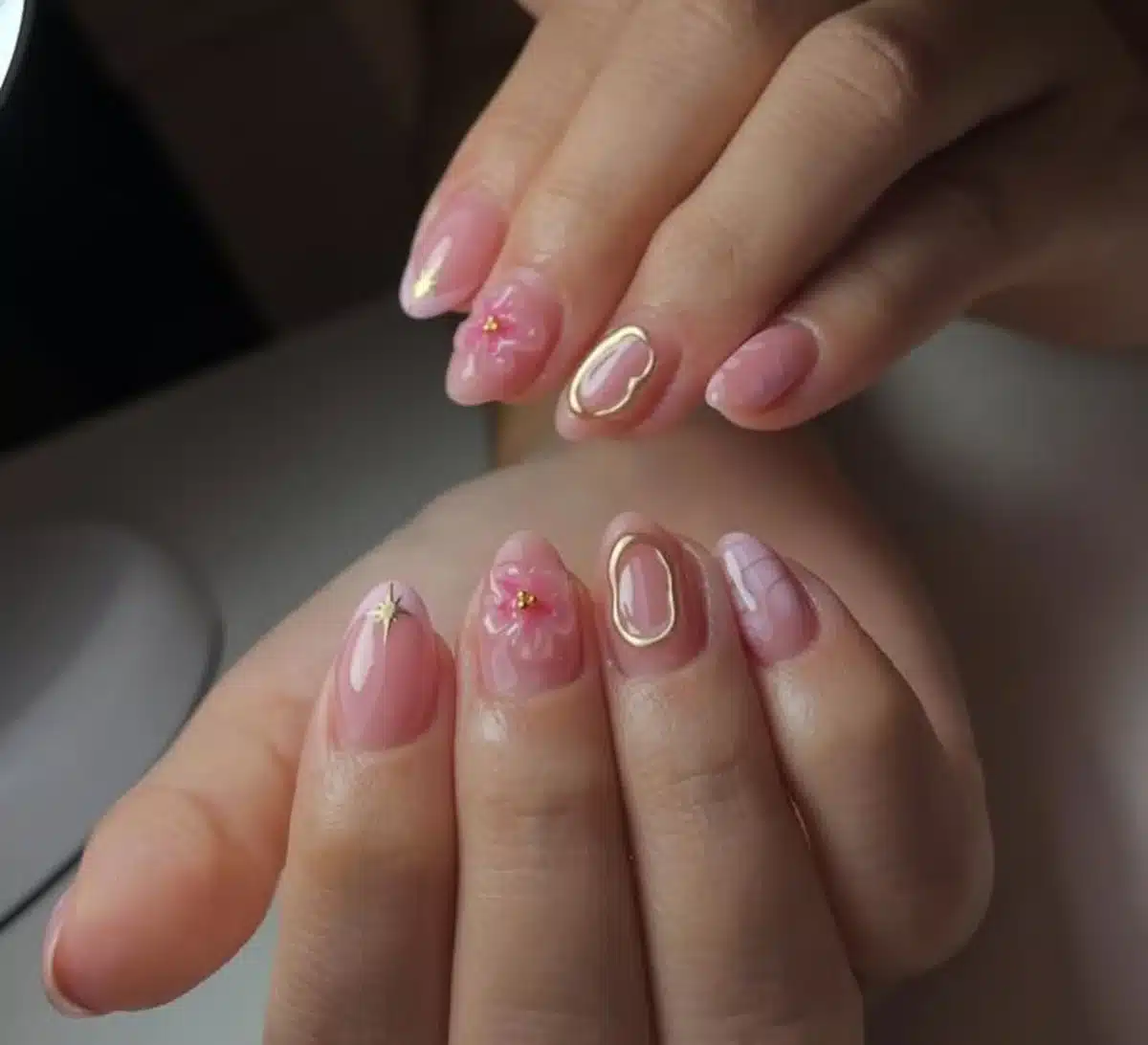 Unhas decoradas com textura em tons de rosa, com flores 3D e contornos dourados