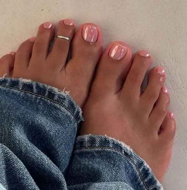 Unhas dos pés cuidadas com esmalte rosa claro e anel no dedo.
