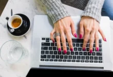 Mulher com unhas lindas e práticas digitando no teclado de um laptop.