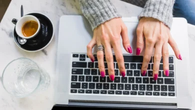 Mulher com unhas lindas e práticas digitando no teclado de um laptop.
