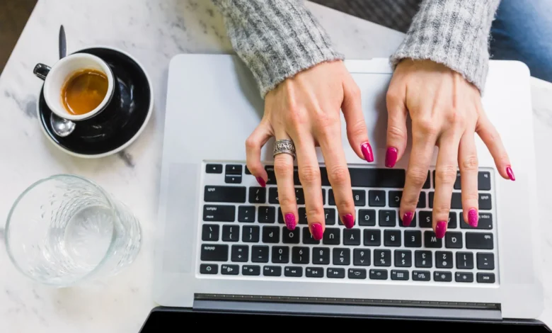 Mulher com unhas lindas e práticas digitando no teclado de um laptop.