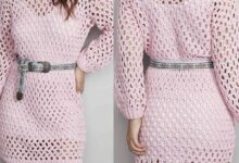 Vestido de crochê rosa com mangas longas e cinto estampado, criando um visual delicado e moderno