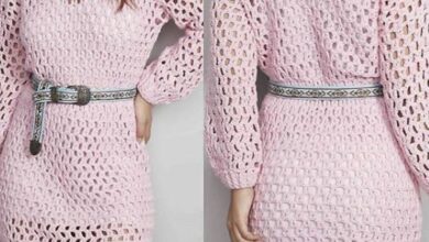 Vestido de crochê rosa com mangas longas e cinto estampado, criando um visual delicado e moderno