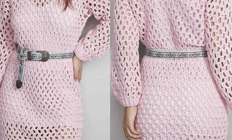 Vestido de crochê rosa com mangas longas e cinto estampado, criando um visual delicado e moderno