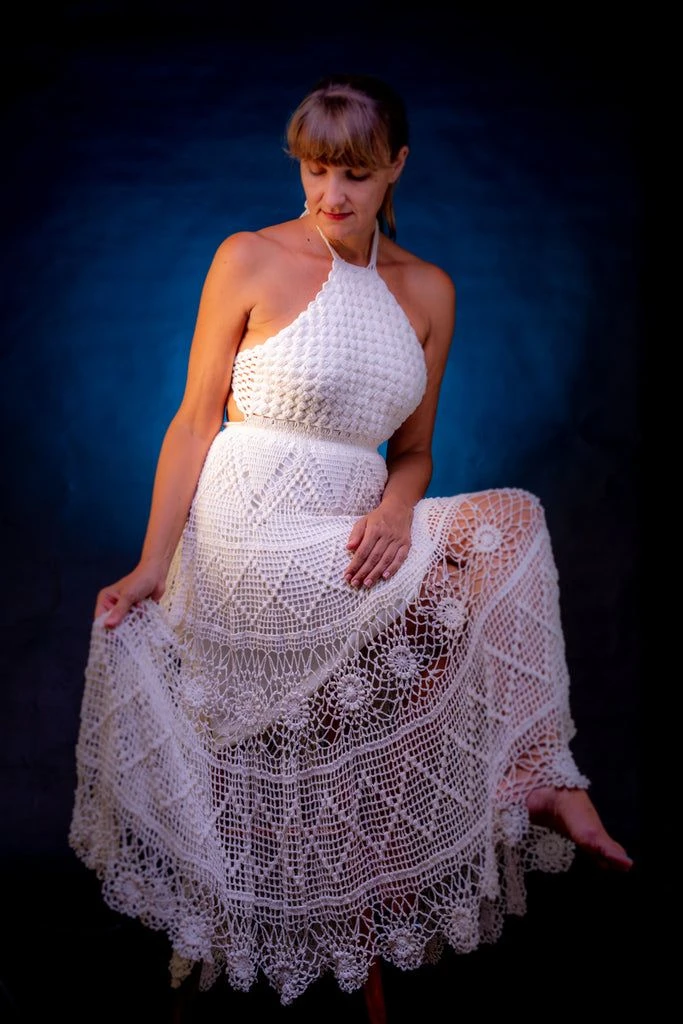 Mulher vestindo vestido longo de crochê branco com detalhes delicados e design elegante.
