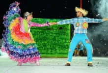 Casal dançando quadrilha com trajes típicos de São João, com chapéu de palha e roupas coloridas.