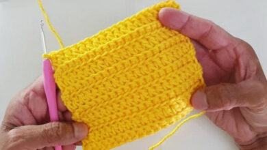 ãos segurando amostra de crochê amarelo vibrante com ponto texturizado, mostrando técnica de crochê fácil com agulha rosa e fio de algodão.