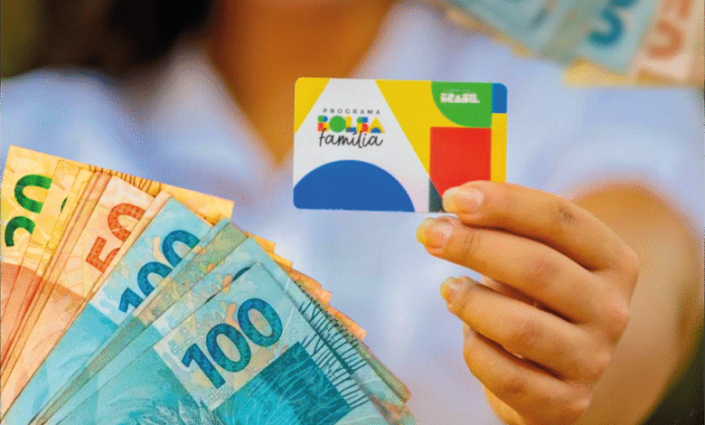 Pessoa segurando o cartão do Bolsa Família com notas de real ao fundo