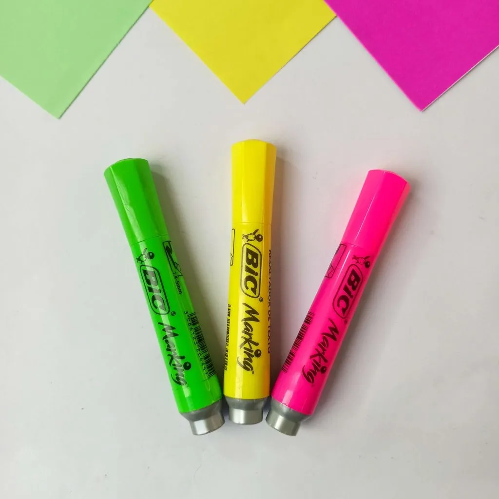 Canetas Pincel Bic nas cores verde, amarelo e rosa, em destaque sobre folhas coloridas